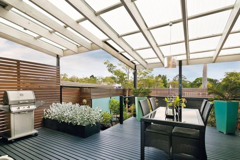 Überdachte Terrasse mit lichtdurchlässigem Dach aus opalen Wellplatten, darunter moderne Gartenmöbel auf Holzdeck – Beispiel für den Einsatz von Lichtplatten bei privaten Überdachungen.